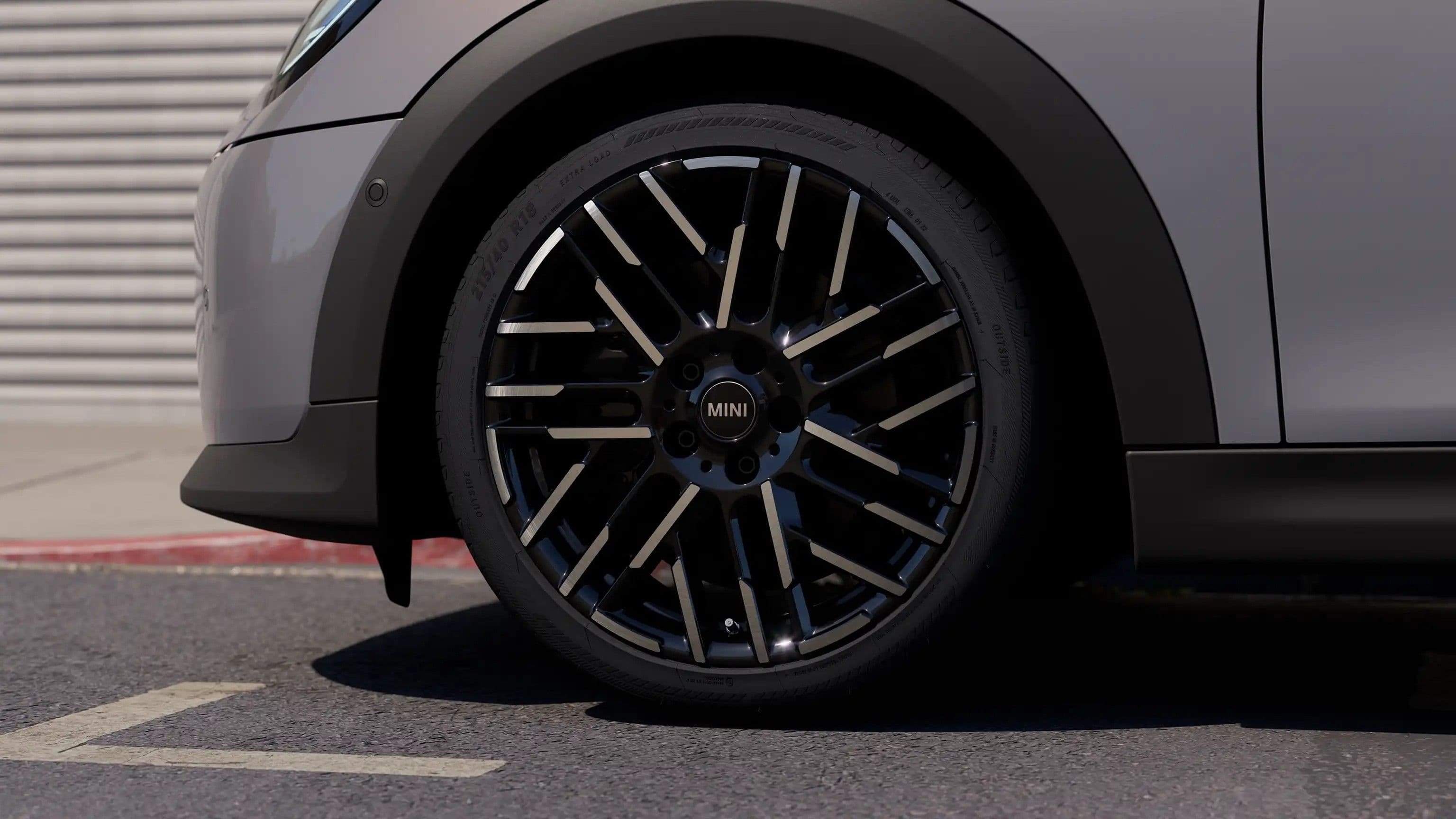 Close-up of a gray Mini Cooper wheel with a black and silver geometric spoke design.