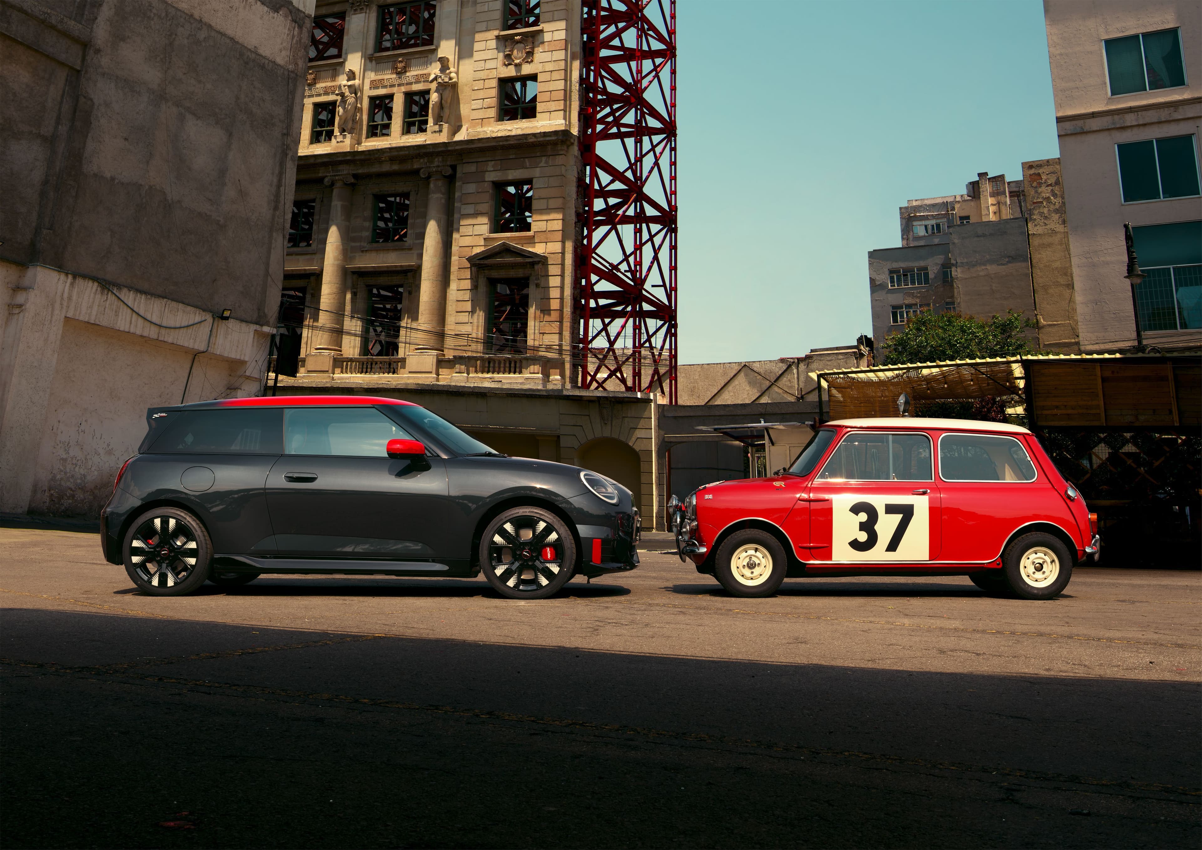 A modern charcoal Mini Cooper S Clubman parked next to a vintage red Mini Cooper with racing number 37.