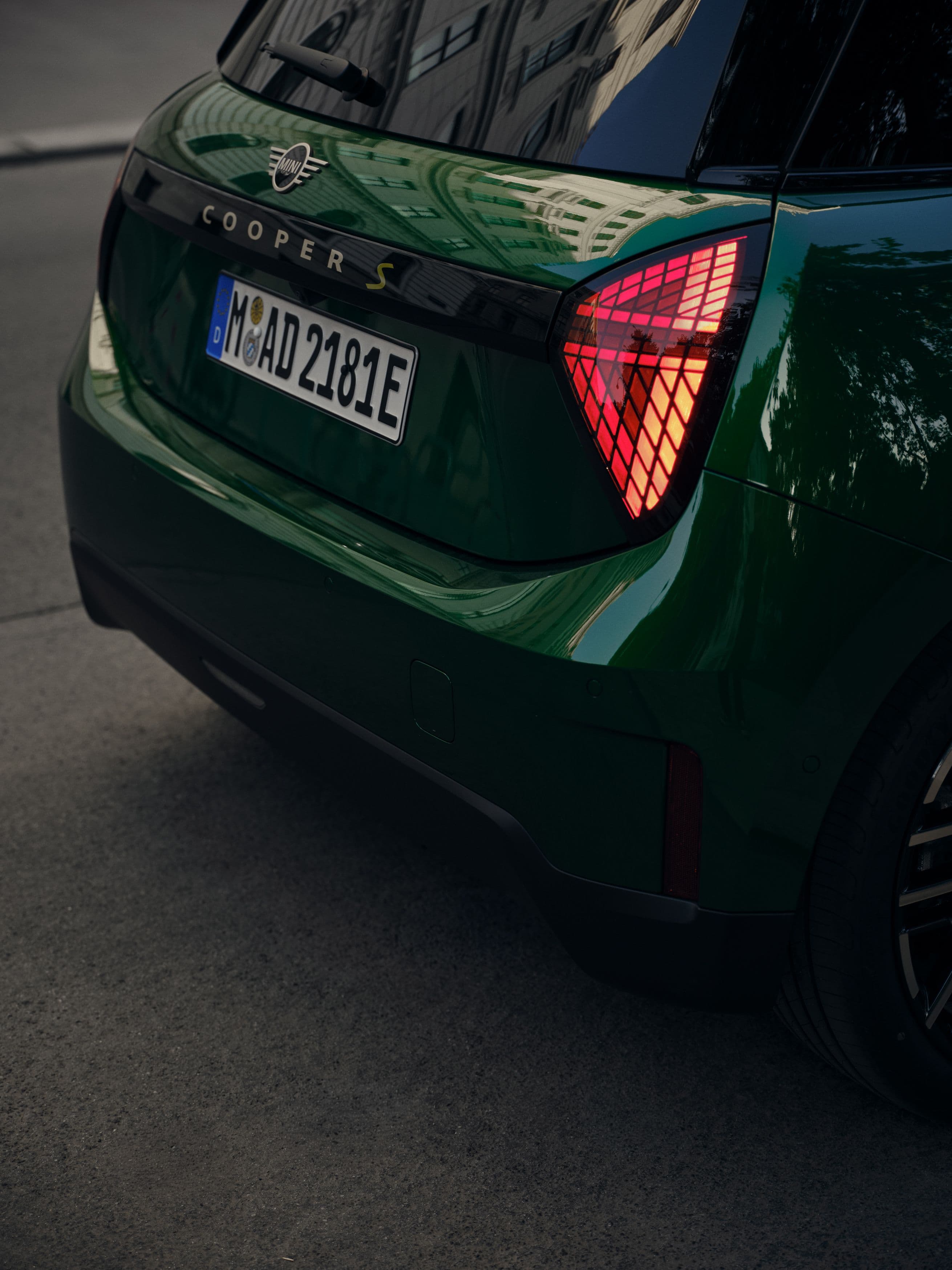Rear view of a dark green electric car with distinctive taillights and a license plate.