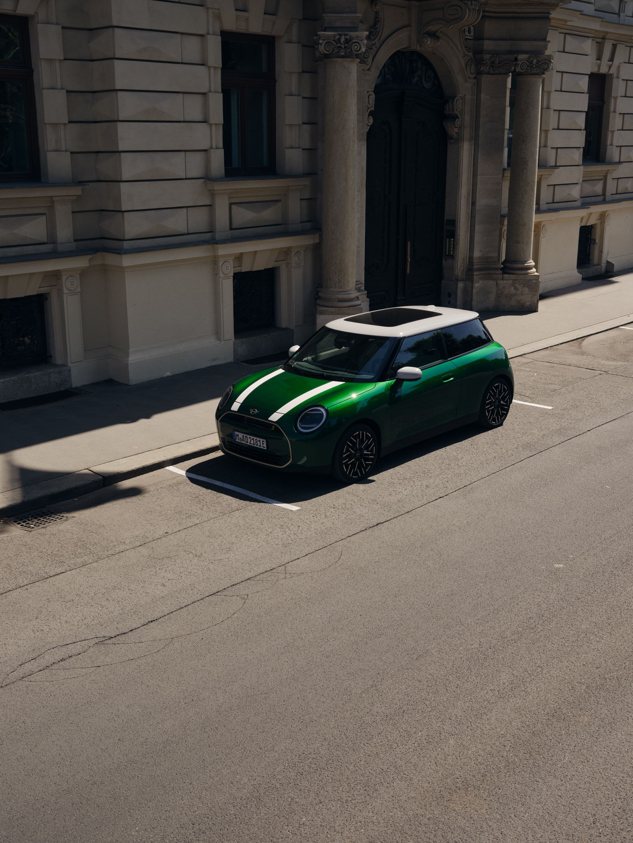 Green Mini Cooper with white racing stripes parked on a city street.