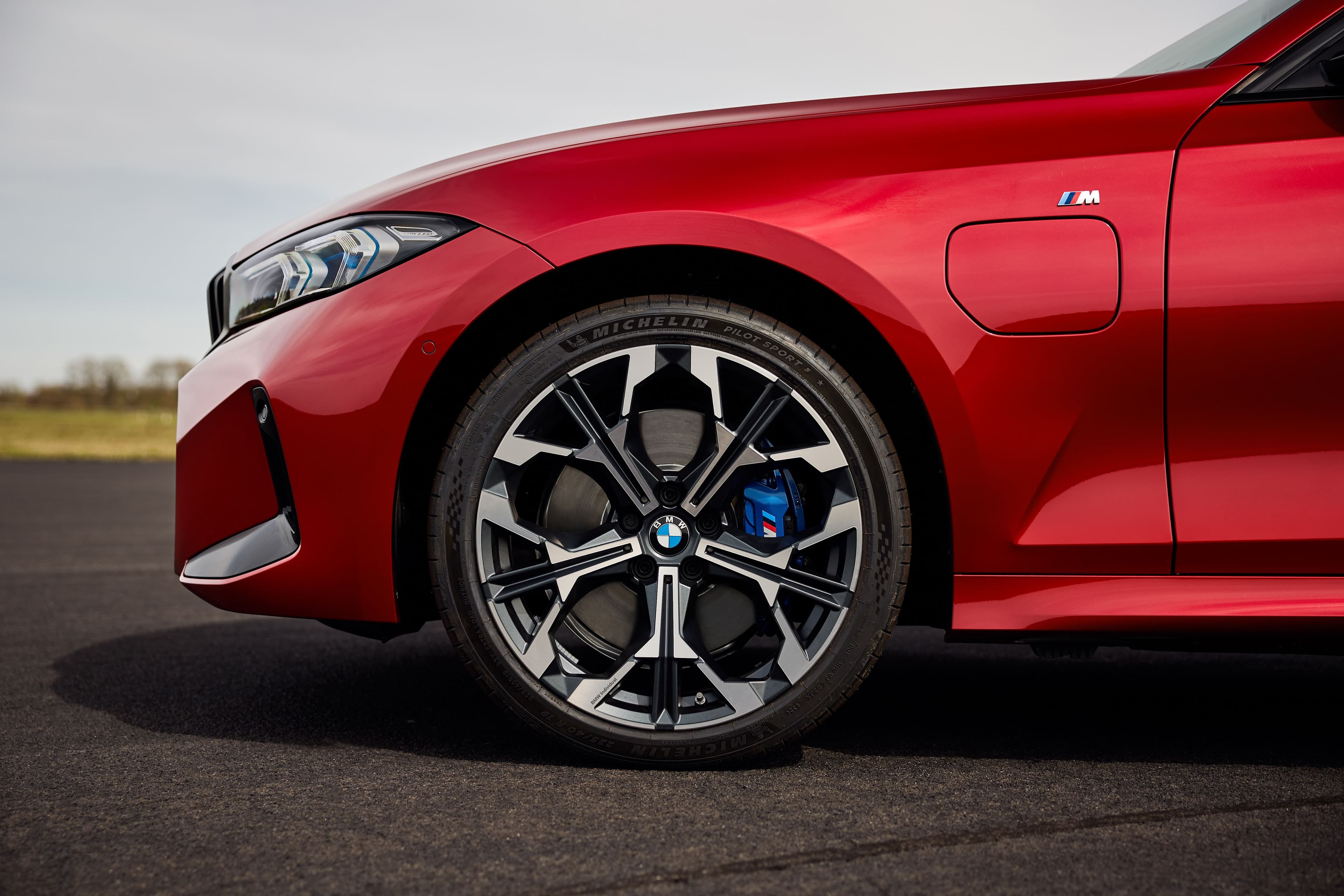 Close-up of a red BMW electric car's front wheel with intricate alloy design and blue brake caliper.
