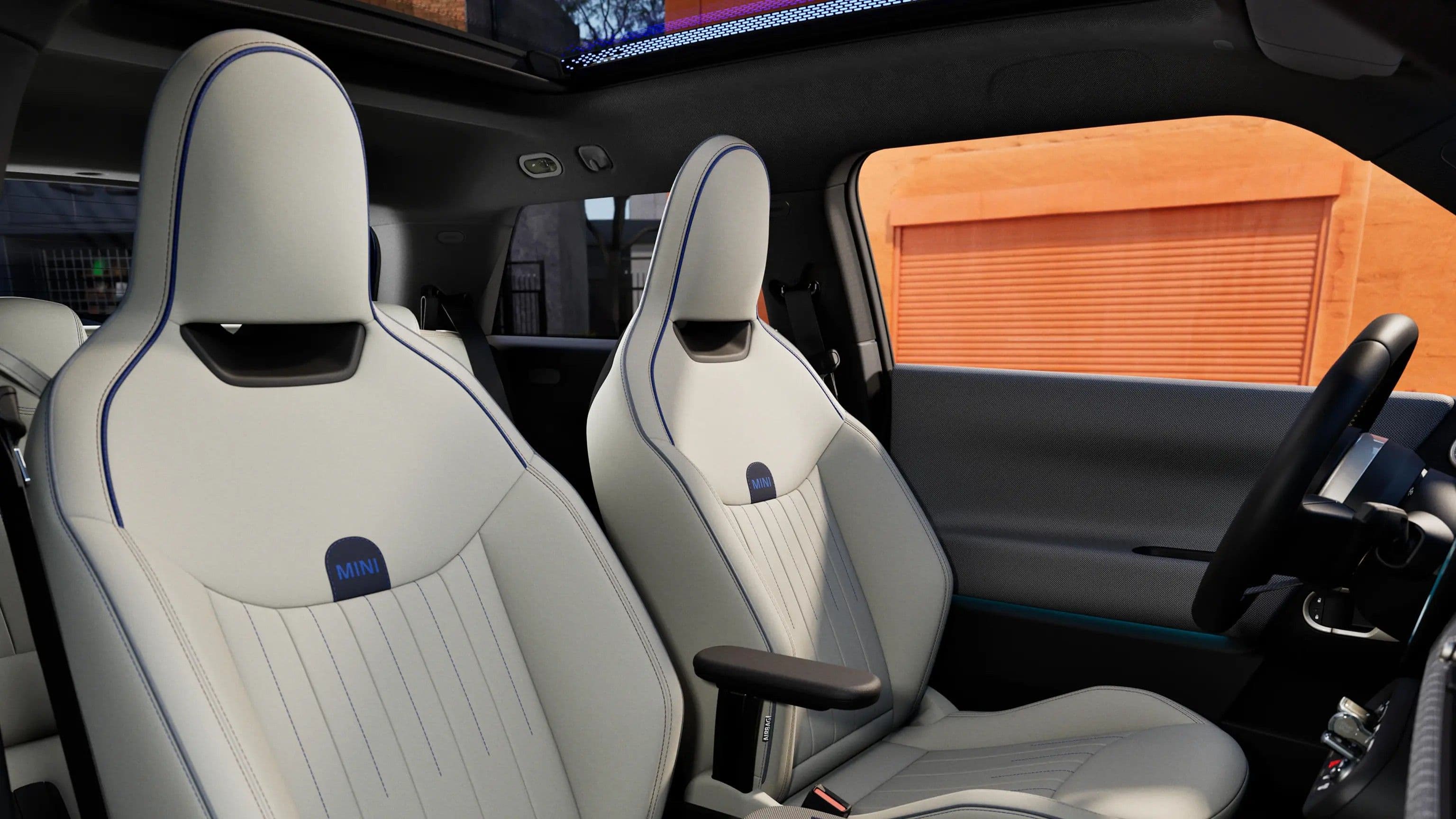 Front seats of a modern car, white leather with blue accents and stitching.