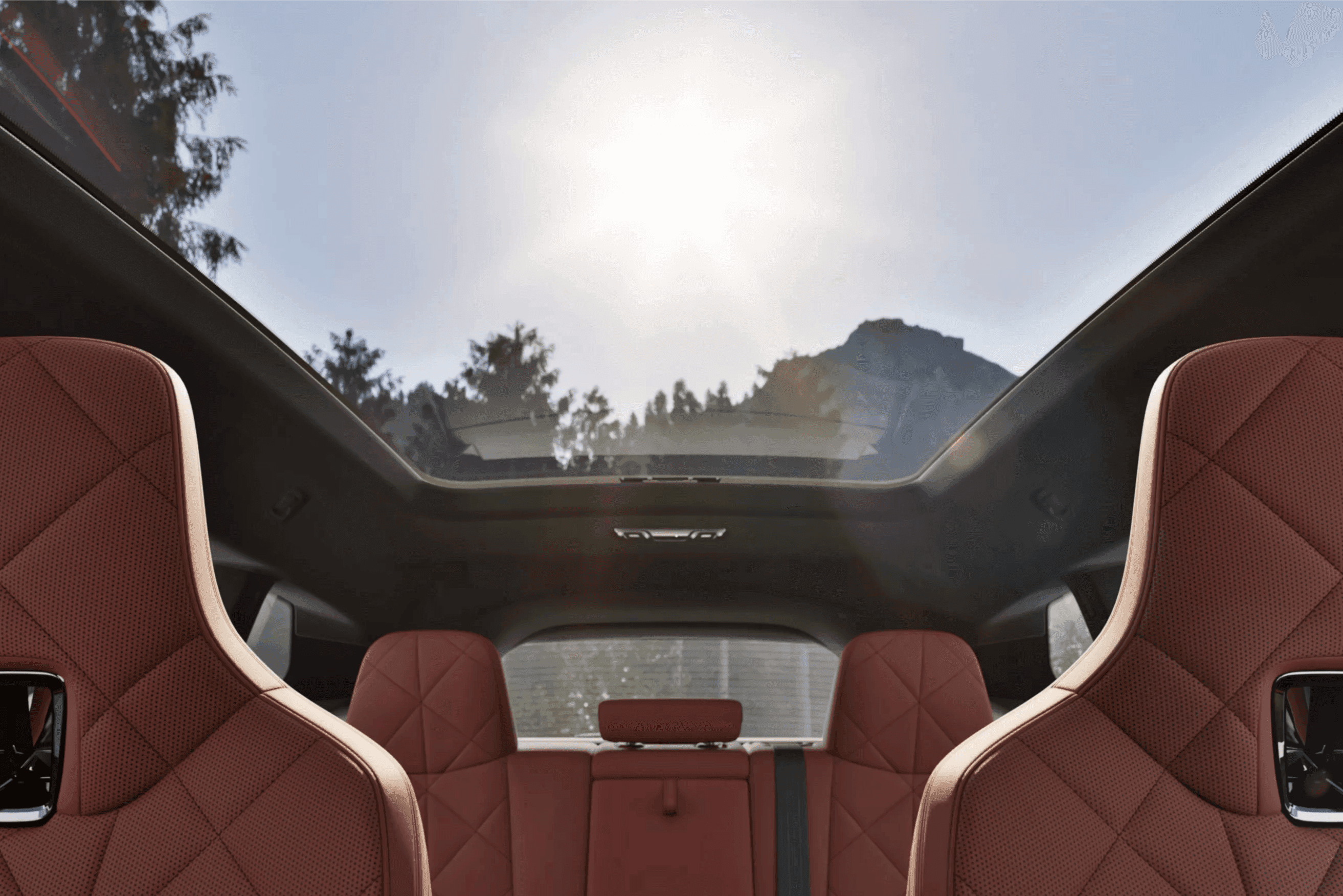 View through the panoramic sunroof of a car, showing sun, trees, and mountains.