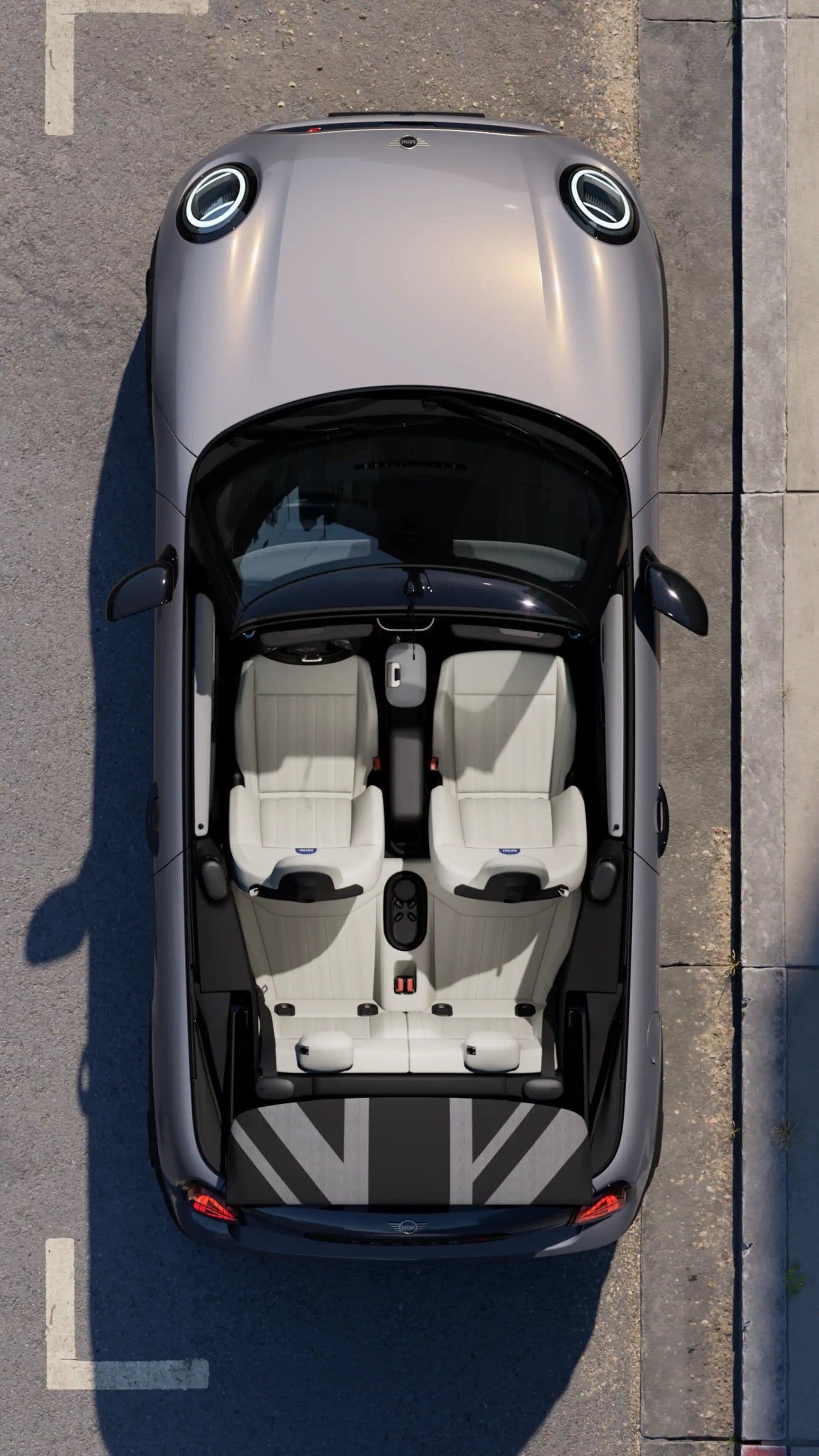 Top-down view of a silver Mini Cooper convertible with the roof down showing light-colored interior and Union Jack pattern in the trunk.