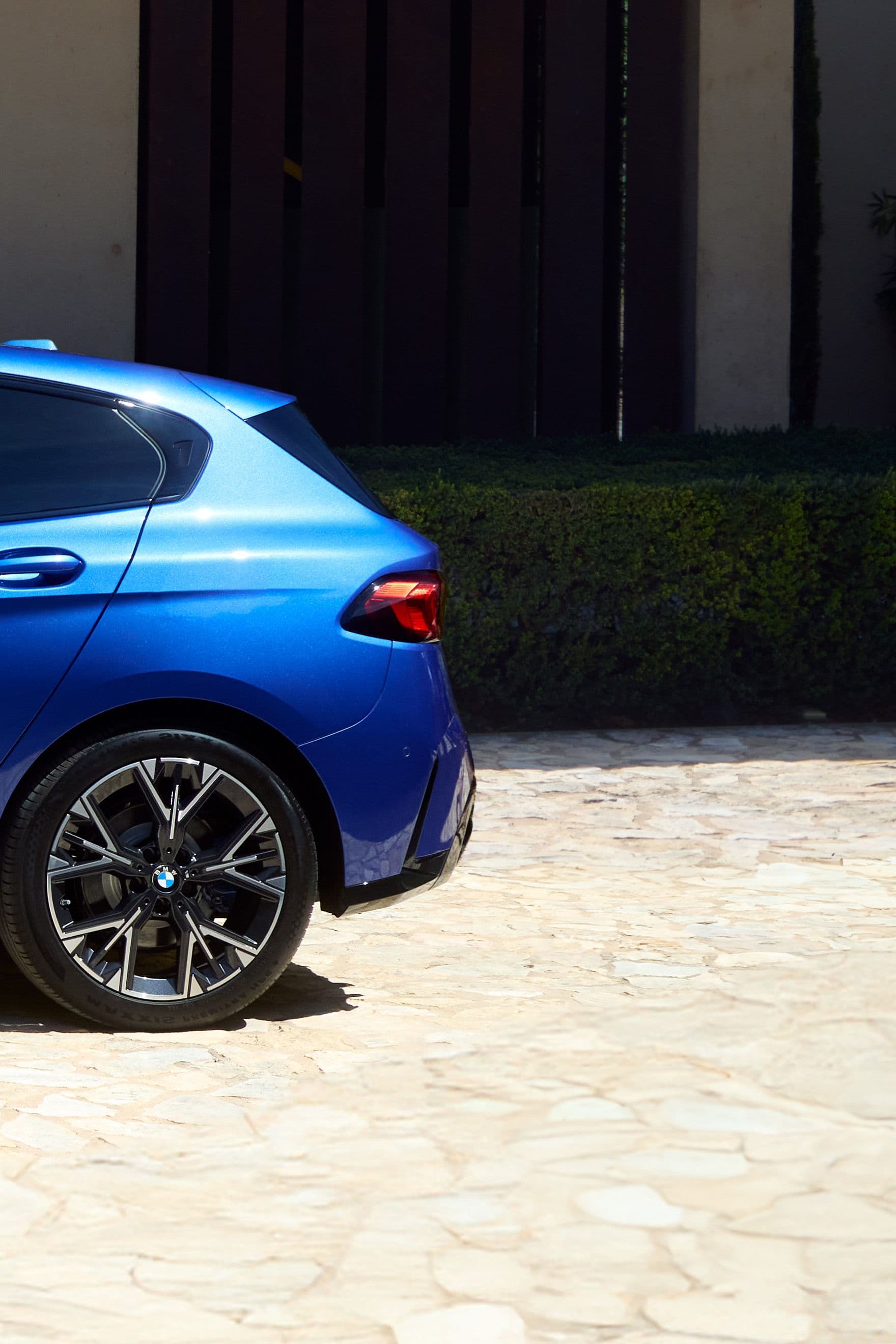 Close-up rear view of a sleek, blue hatchback car with tinted windows and stylish alloy wheels parked on a gravel driveway.