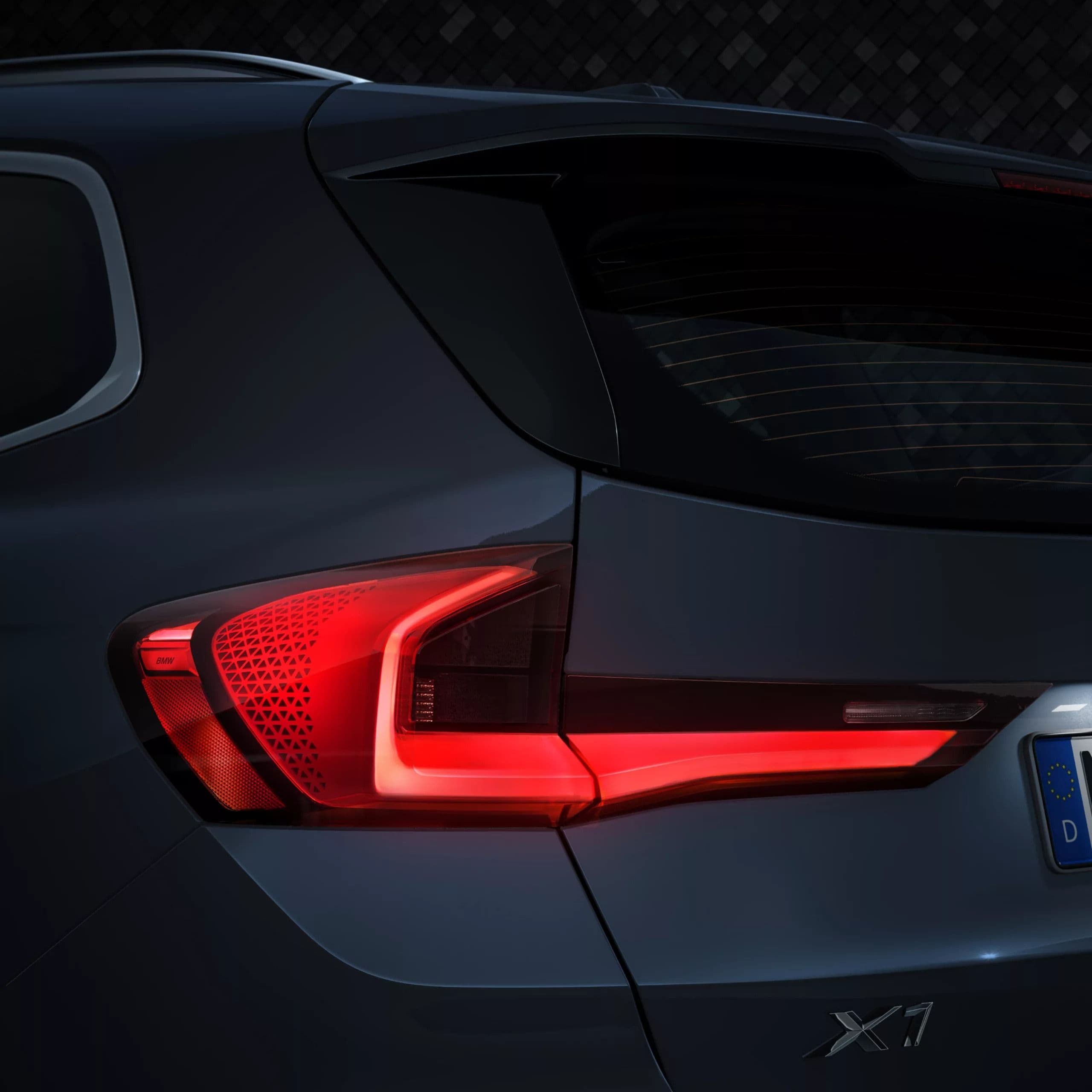 Close-up of a dark gray BMW X1's rear left taillight illuminated at night.