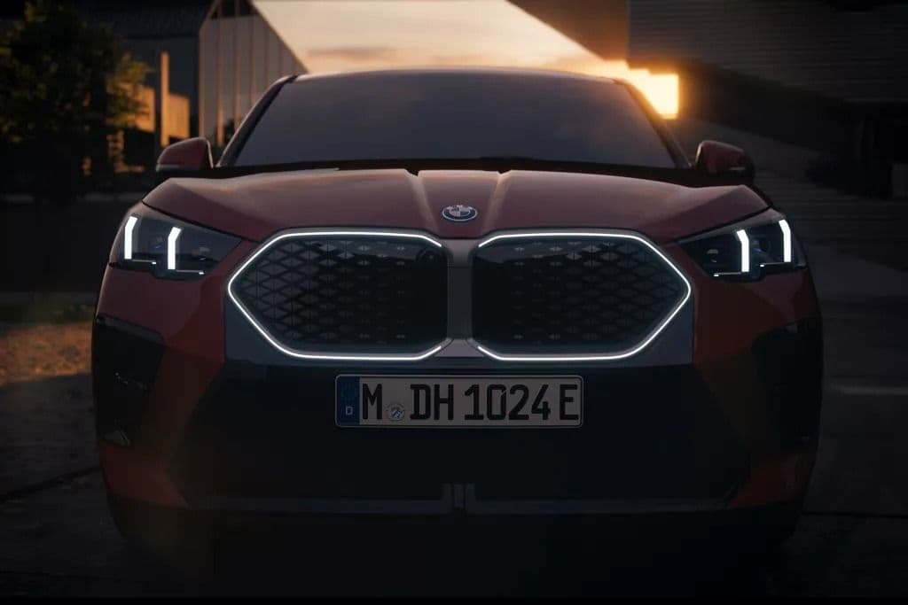 Red BMW iX2 with illuminated grille and headlights at dusk.