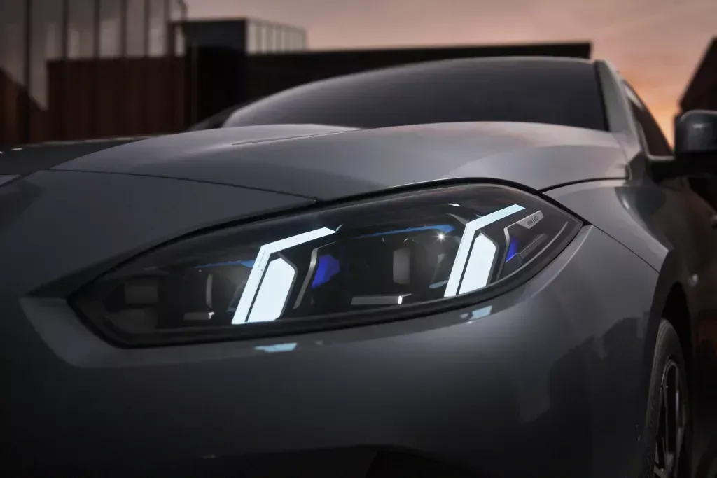 Close-up of a modern gray car's illuminated LED headlight at dusk.