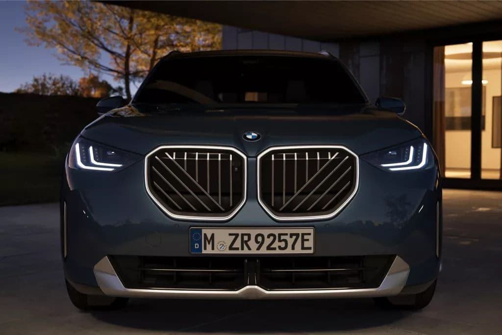Front view of a dark blue BMW iX electric SUV with illuminated kidney grille and headlights.