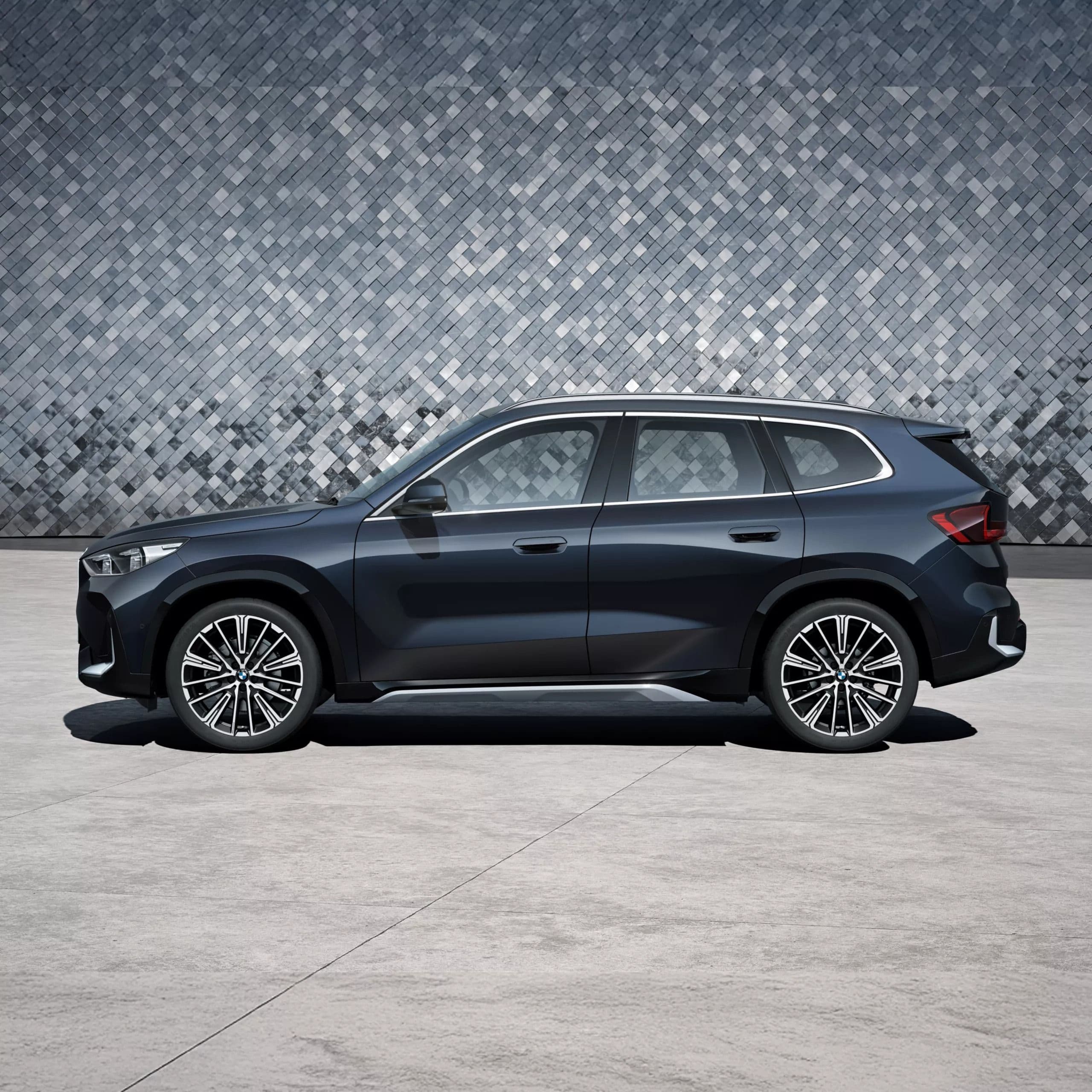 Dark blue BMW X1 SUV parked on a concrete surface with a textured wall behind it.